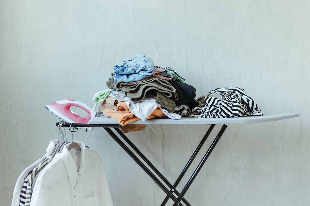 Neatly arranged ironing board with iron, sorted clothes, and hanging white shirts.