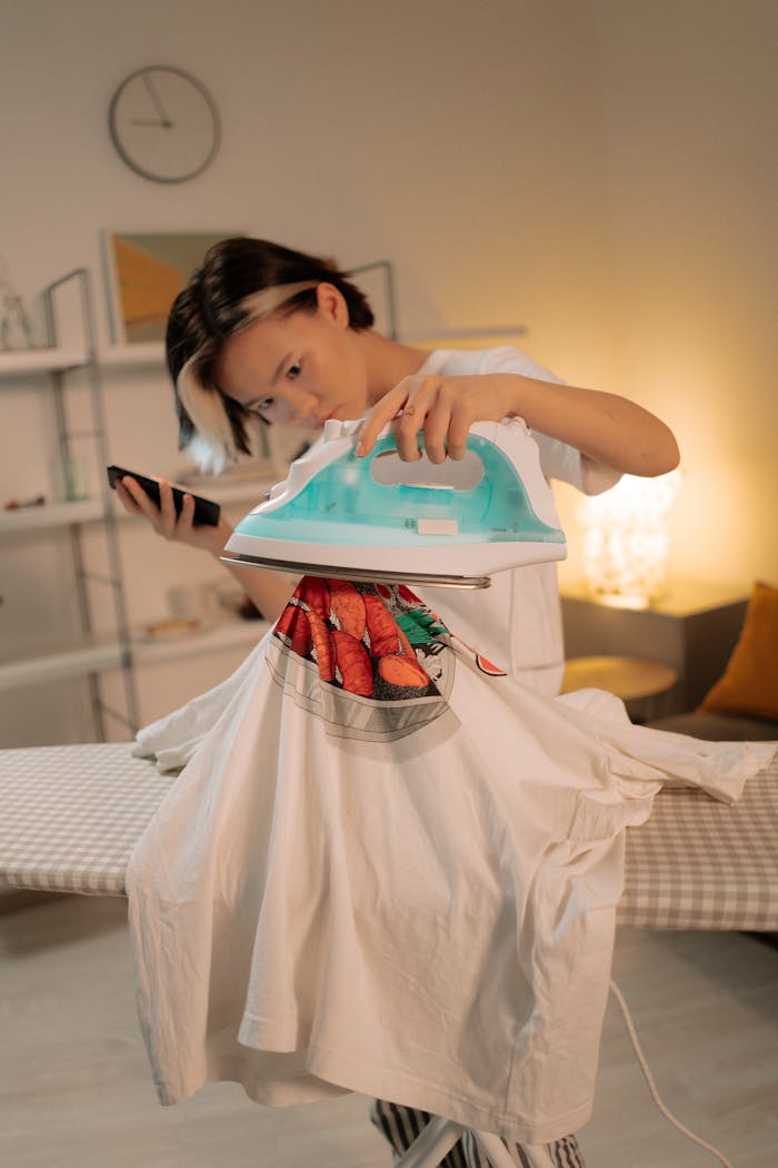 A woman multitasking by ironing a shirt and using a smartphone indoors.